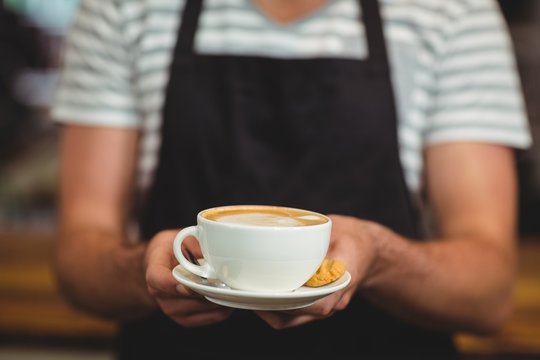 Mid section of waiter offering a cup of coffee