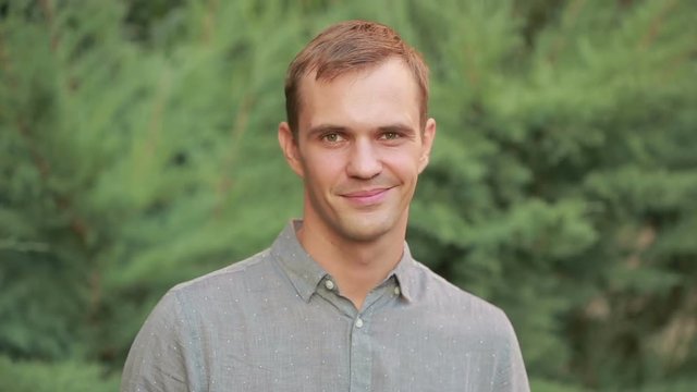 Young man smiling with yellow teeth. Vibrant green leaves as a background.