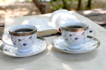  open book, two design cups of coffee on the wooden table in sunny day in the forest and mobile phone 