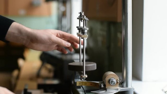 white man's hand puts weight on a pendulum in physics laboratory. It leads the pendulum in motion. The pendulum rotates at a constant period. Hand stops the pendulum. It removes the weight