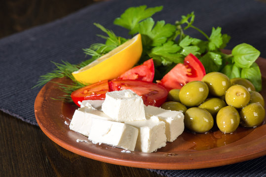 feta cheese, tomatoes, olives and herbs in a clay plate