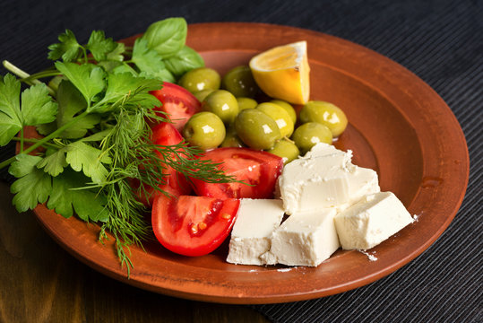 feta cheese, tomatoes, olives and herbs in a clay plate