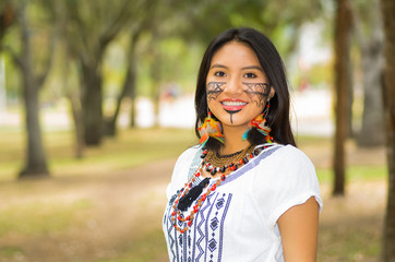 Beautiful Amazonian woman with indigenous facial paint and white traditional dress posing happily...
