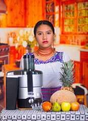 Charming young woman in traditional andean dress standing inside kitchen posing in front of juice maker, healthy lifestyle concept