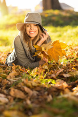 Happy young woman with leaves in park in autumn