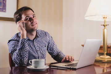 Young happy man talking on the phone at his workplace in office