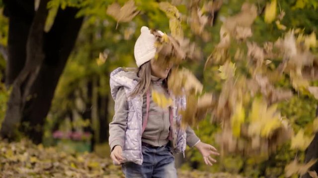 Little cute girl throws fallen leaves in autumn park