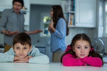 Upset children sitting while couple arguing with each other