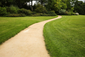 Fototapeta na wymiar Long white curved garden path surrounded by lush foliage