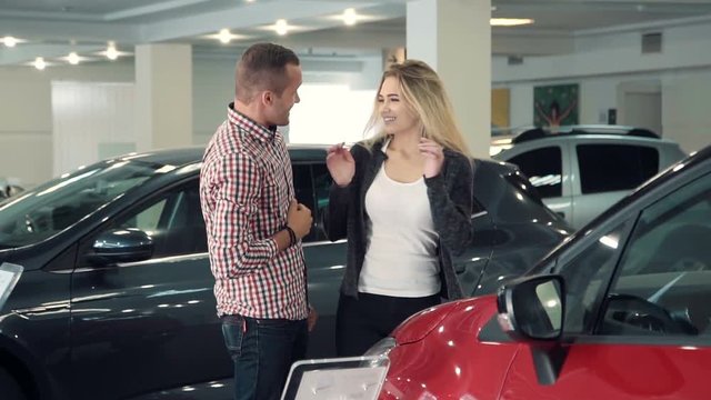 Slowmotion Man Standing Behind Woman and Covering Her Eyes While Standing in front of Shiny New Red Vehicle Inside Car Dealership