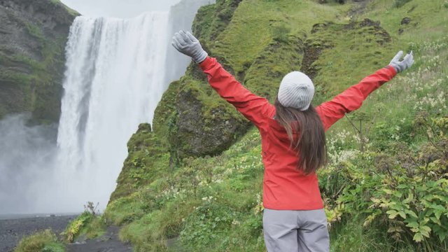 Waterfall - Happy woman by Skogafoss on Iceland serene and free outdoors. Girl visiting famous tourist attractions and landmarks in Icelandic nature landscape on the ring road. RED EPIC SLOW MOTION