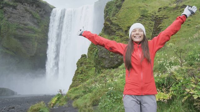 Blissful woman by waterfall Skogafoss joyful and happy turning and spinning dancing in bliss and joy on Iceland. Girl visiting tourist attraction and landmark in Icelandic nature on the ring road.
