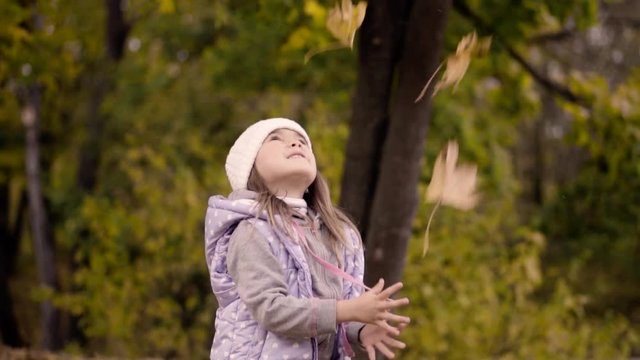 Little cute girl throws fallen leaves in autumn park