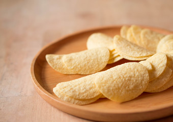 Fried crispy potatoes chips on round wood plate  background