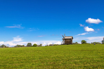 Fototapeta premium Rural landscape. Traditional wooden windmill on green hill. Kizhi Island. Karelia, Russia. UNESCO heritage landmark