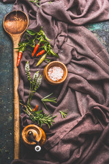 Aged wooden cooking spoon with spices, pepper mill and salt on crumpled tablecloth, top view