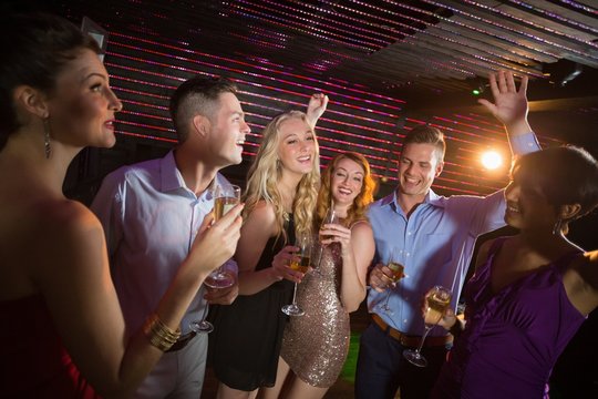 Smiling friends holding glasses of champagne while dancing