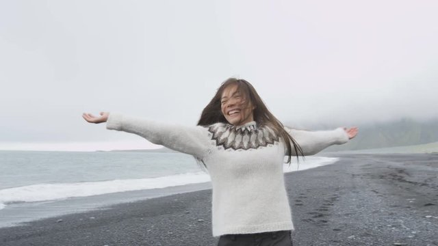 Dancing free happy woman on Iceland dancing of joy in Icelandic sweater on black sand beach. Joyful girl happy swirling around smiling outdoors in nature laughing having fun. RED EPIC 90 FPS.