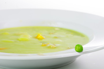 Fresh green pea on the edge of a white plate with vegetable soup