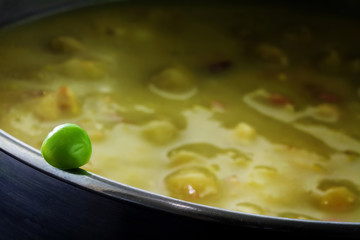 Fresh green pea on the edge of a pot full with overcooked vegetable soup