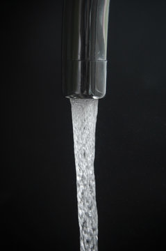 Aerated water flowing from a tap surrounded by floating droplets on dark background