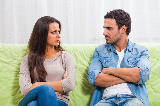 Young couple is sitting on sofa at home. They are angry and not talking to each other.