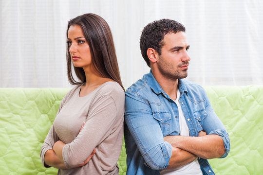 Young couple is sitting on sofa at home. They are angry and not talking to each other.