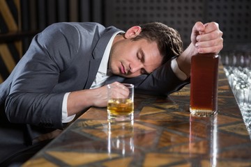 Drunk man lying on a counter with bottle of whisky