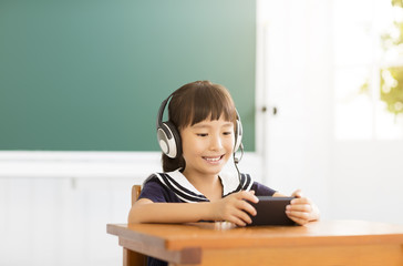 Naklejka premium happy little girl learning with smart phone in classroom