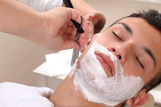 Shaving at the barber of a young boy in retro style with razor and shaving soap