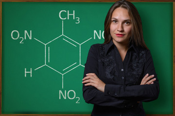 Beautiful young girl (teacher, schoolgirl, student or business woman) posing near a school blackboard with the inscription chemical formula
