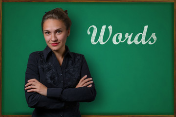 Beautiful young woman teacher (student, business woman) in classical dress standing near a blackboard with the inscription