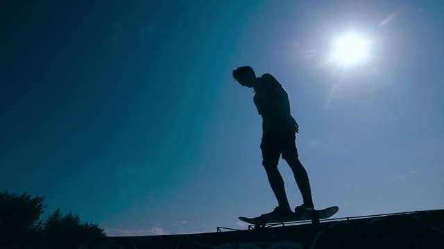 Skateboarder silhouette skateboarding on a sky background at sunset. Slow motion. HD.
