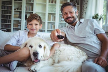 Father and son sitting with pet dog and watching televis