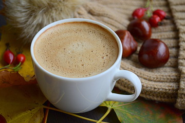 Cup of coffee with leaves, chestnuts and faux fur pompon hat