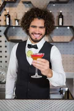 Bartender holding glass of cocktail in bar counter