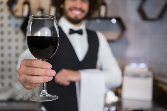 Bartender serving glass of red wine in bar counter