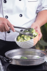 Chef putting broccoli hot water with tongs