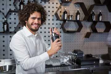 Fototapeta na wymiar Happy waiter shaking drink in cocktail shaker in a bar