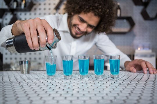 Bartender pouring cocktail into shot glasses