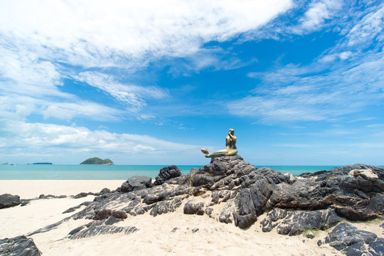 Seascape of sky and beach which has mermaid statue on rock ; Son