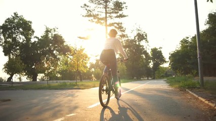 back view woman riding a bicycle through the park in sunlight - Powered by Adobe