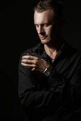Portrait of a handsome man in a black shirt in the Studio with a Cup of tea