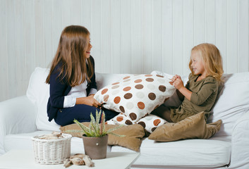 two cute sisters at home playing, little girl in house interior on sofa, messing hair, fighting...