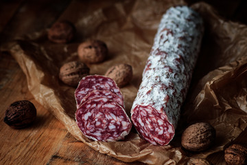 Italian salami with walnuts on craft paper on rustic  wooden background.