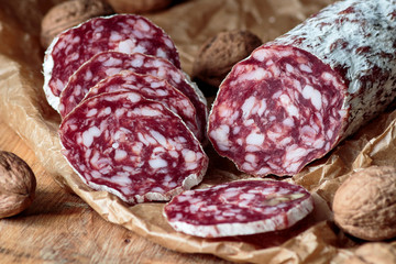 Italian salami with walnuts on craft paper on rustic  wooden background.