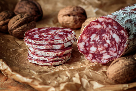 Italian salami with walnuts on craft paper on rustic  wooden background.