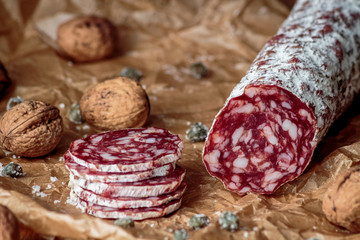 Italian salami with walnuts on craft paper on rustic  wooden background.