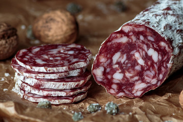 Italian salami with walnuts on craft paper on rustic  wooden background.