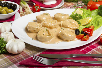 Salmon tortellini in sauce served on a white plate with lemon, olives, cherry tomatoes and parsley next to fresh garlic.